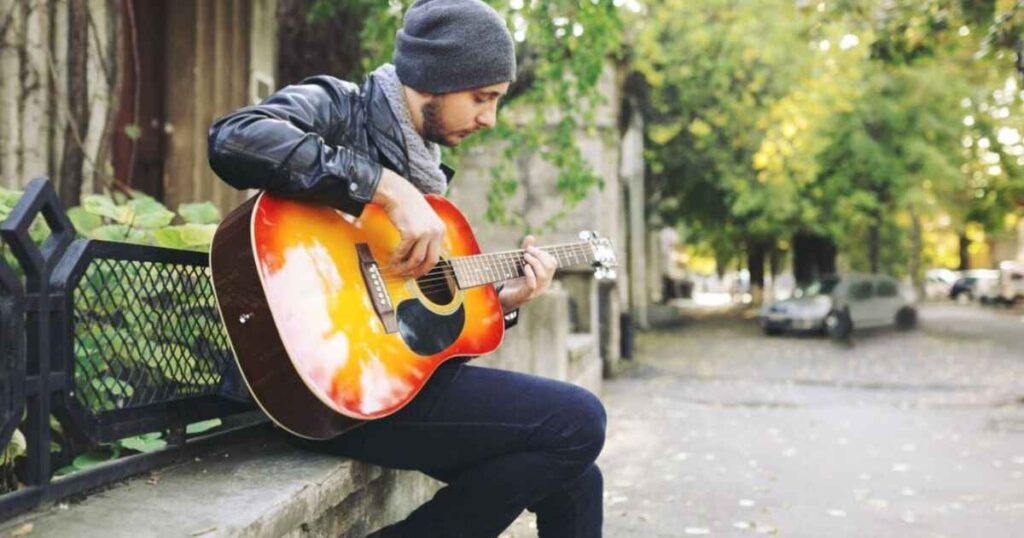 A man sits on a bench, strumming an acoustic guitar, embodying the essence of Street Life on Honcho's Music.