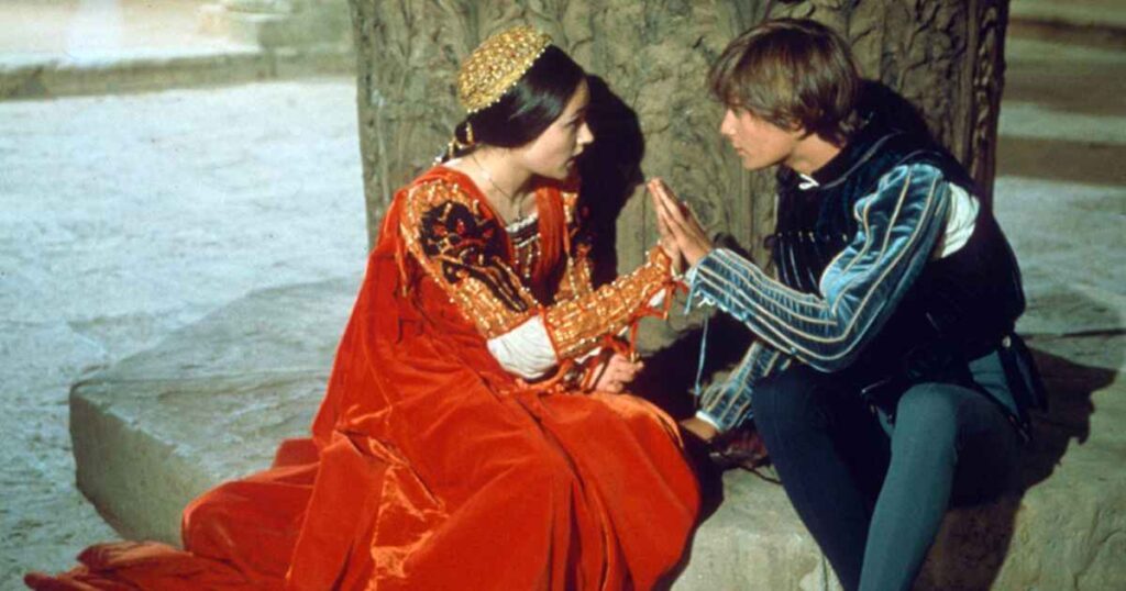 A man and woman in medieval attire seated on a stone, reflecting the background on the songs' creation for Romeo and Juliet 1996.