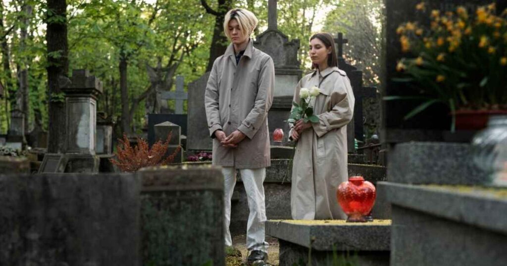 A man and woman stand solemnly in a cemetery, reflecting on life and loss, embodying themes from "the-meaning-of-my-ordinary-life-by-the-living-tombstone."